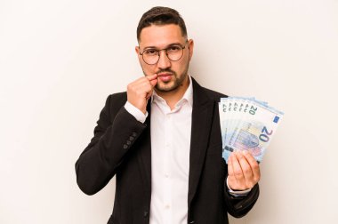 Latin kökenli bir adamın elinde banknotlar var. Beyaz arka planda izole edilmiş ve parmakları dudaklarında bir sır saklıyor..