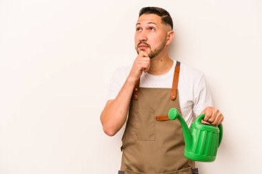 Bahçıvan, elinde su dolu bir teneke kutu tutan İspanyol şüpheli ve şüpheci bir ifadeyle beyaz arka plana bakıyor..