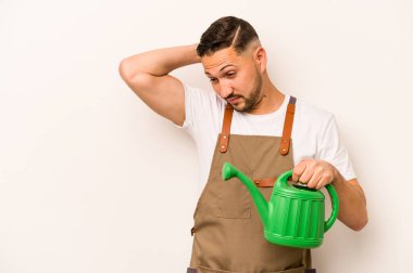 Bahçıvan İspanyol bir adam elinde su kovası tutarak beyaz arka planda izole edilmiş kafasının arkasına dokunuyor, düşünüyor ve bir seçim yapıyor..