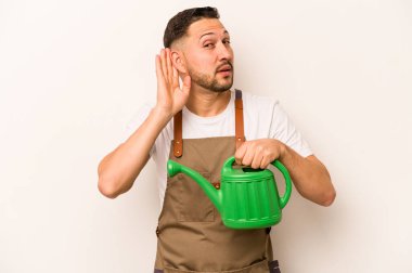 Bahçıvan İspanyol, elinde su bidonu olan bir adam beyaz arka planda izole edilmiş bir şekilde bir dedikoduyu dinlemeye çalışıyor..