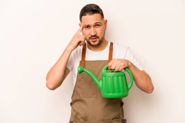 Bahçıvan İspanyol bir adam beyaz arka planda izole edilmiş bir su kabı tutuyor. Parmağıyla tapınağı işaret ediyor, düşünüyor, bir göreve odaklanıyor..