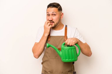Bahçıvan, elinde su dolu bir teneke tutarak beyaz arka planda izole edilmiş tırnak yiyen sinirli ve endişeli bir adam..