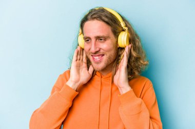 Genç beyaz adam mavi arka planda izole edilmiş müzik dinliyor.