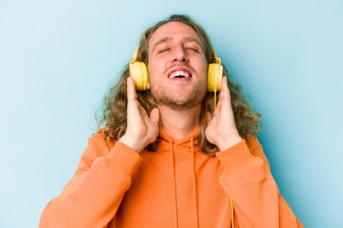 Genç beyaz adam mavi arka planda izole edilmiş müzik dinliyor.