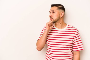 Beyaz arka planda izole edilmiş genç bir İspanyol şüpheli ve şüpheci bir ifadeyle yana bakıyor..