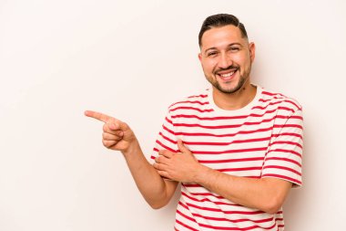 Beyaz arka planda izole edilmiş genç İspanyol adam işaret parmağıyla işaret ederek gülümsüyor..