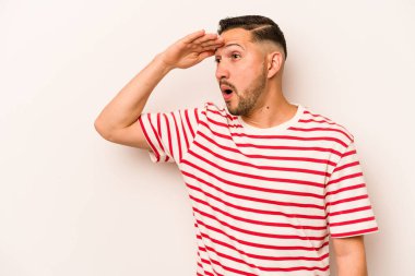 Beyaz arka planda izole edilmiş genç İspanyol adam uzaklara bakıyor ve elini alnına koyuyor..