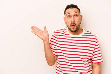 Beyaz arka planda izole edilmiş genç İspanyol adam, avuç içinde kopya alanı tutmaktan etkilenmiş..