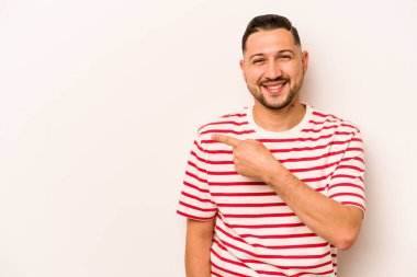 Beyaz arka planda izole edilmiş genç İspanyol adam gülümsüyor ve boş alanda bir şeyler gösteriyor..