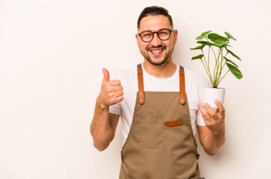 İspanyol bahçıvan elinde bir bitki tutuyor. Beyaz arka planda izole edilmiş. Gülümsüyor ve başparmağını kaldırıyor.