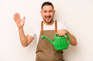 Bahçıvan İspanyol bir adam beyaz arka planda izole edilmiş bir su bidonu tutuyor. Hoş bir sürpriz alıyor, heyecanlı ve el kaldırıyor..