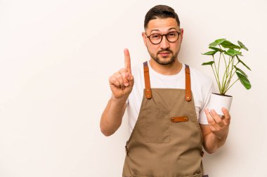 İspanyol bahçıvan elinde bir bitki tutuyor. Beyaz arka planda bir numarayı parmağıyla gösteriyor..