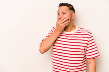 Genç İspanyol bir adam beyaz arka planda izole edilmiş. Düşünceli bir şekilde bir fotokopi odasına bakıyor. Ağzını eliyle kapatıyor..