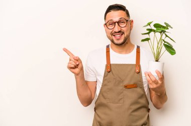 Beyaz arka planda izole edilmiş bir bitki tutan İspanyol bahçıvan gülümsüyor ve boş alanda bir şey gösteriyor..