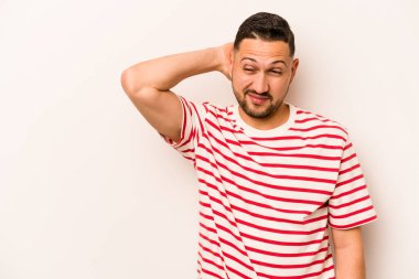 Genç İspanyol bir adam beyaz arka planda izole edilmiş kafasının arkasına dokunuyor, düşünüyor ve bir seçim yapıyor..