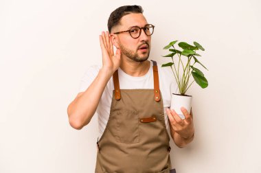 Beyaz arka planda bir bitki tutan İspanyol bahçıvan bir dedikoduyu dinlemeye çalışıyor..