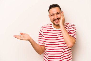 Beyaz arka planda izole edilmiş genç İspanyol bir adam avuç içinde fotokopi alanı tutuyor, el üstünde tutuyor. Şaşırmış ve mutlu..