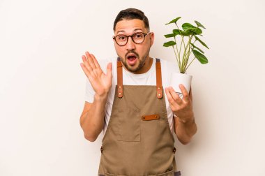 İspanyol bahçıvan elinde bir bitki tutuyor. Beyaz arka planda izole edilmiş. Şaşırmış ve şok olmuş..