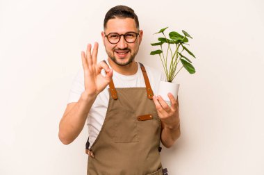 İspanyol bahçıvan elinde bir bitki tutuyor. Beyaz arka planda izole edilmiş. Neşeli ve kendinden emin..