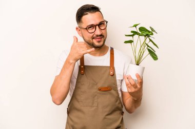 Beyaz arka planda izole edilmiş bir bitki tutan İspanyol bahçıvan parmaklarıyla bir cep telefonu hareketi gösteriyor..
