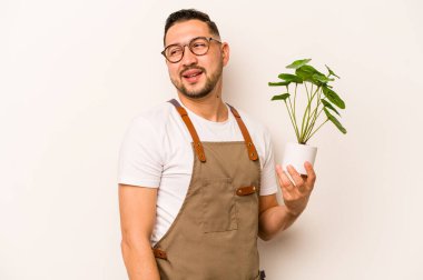 Beyaz arka planda izole edilmiş bir bitki tutan İspanyol bahçıvan gülümseyen, neşeli ve keyifli bir kenara bakar..