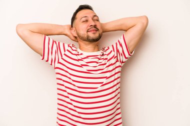 Beyaz arka planda izole edilmiş genç İspanyol bir adam kendini güvende hissediyor, elleri başının arkasında..