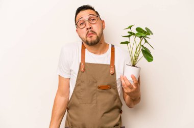 Beyaz arka planda izole edilmiş bir bitki tutan İspanyol bahçıvan omuzlarını silker ve gözleri açık kalır..