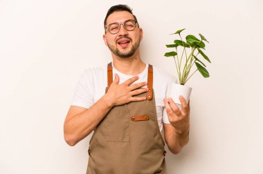 Beyaz arka planda izole edilmiş bir bitki tutan İspanyol bahçıvan elini göğsünde tutarak kahkaha atıyor..