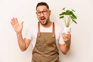 Beyaz arka planda bir bitki tutan İspanyol bahçıvan hoş bir sürprizle karşılaşıyor, heyecanlı ve el kaldırıyor..