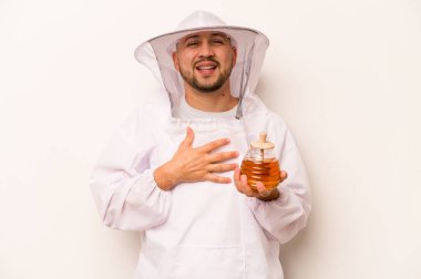 Beyaz arka planda izole edilmiş bal tutan İspanyol arıcı elini göğsünde tutarak kahkahalar atıyor..