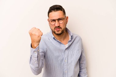 Beyaz arka planda izole edilmiş genç İspanyol adam kameraya yumruk gösteriyor, agresif yüz ifadesi..