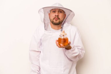 Beyaz arka planda izole edilmiş bal tutan İspanyol arı yetiştiricisi omuz silker ve gözleri açık kalır..