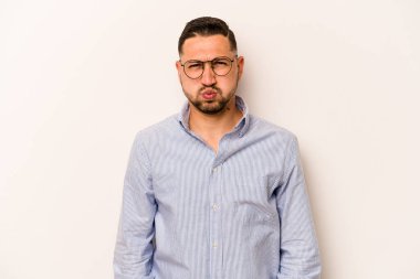 Beyaz arka planda izole edilmiş genç İspanyol adam yanakları patlatıyor, yorgun bir ifadesi var. Yüz ifadesi kavramı.