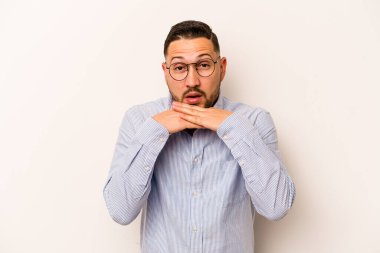 Latin kökenli genç bir adam beyaz arka planda izole edilmiş şans için dua ediyor, şaşırmış ve ağzı açık bir şekilde önüne bakıyor..