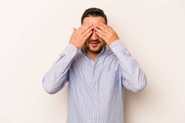 Beyaz arka planda izole edilmiş genç İspanyol adam elleriyle gözlerini kapatmaktan korkuyor..