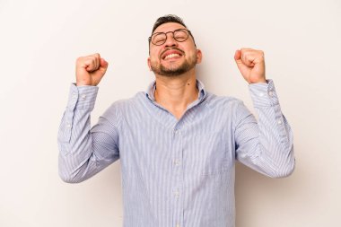 Beyaz arka planda izole edilmiş genç İspanyol bir adam zaferi, tutkuyu ve coşkuyu kutluyor, mutlu bir ifade..