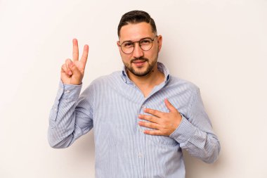Genç İspanyol bir adam beyaz arka planda izole edilmiş yemin ediyor, elini göğsüne koyuyor..
