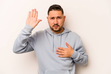 Genç İspanyol bir adam beyaz arka planda izole edilmiş yemin ediyor, elini göğsüne koyuyor..