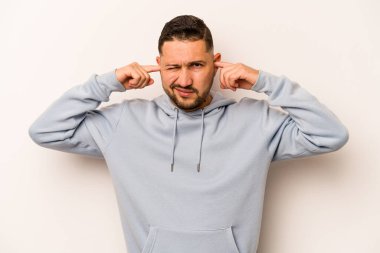 Beyaz arka planda izole edilmiş, kulakları parmaklarla kaplayan, stresli ve çaresiz genç bir İspanyol..