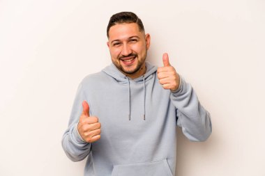 Beyaz arka planda izole edilmiş genç bir İspanyol. Baş parmağını kaldırıyor, gülümsüyor ve kendinden emin..