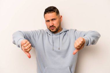 Beyaz arka planda izole edilmiş genç İspanyol adam baş parmağını aşağı gösteriyor ve hoşlanmadığını ifade ediyor..