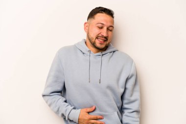 Beyaz arka planda izole edilmiş genç İspanyol adam karnına dokunuyor, nazikçe gülümsüyor, yemek yiyor ve tatmin oluyor..