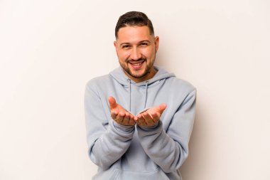Beyaz arka planda izole edilmiş genç İspanyol bir adam avuçlarıyla bir şey tutuyor ve kameraya sunuyor..