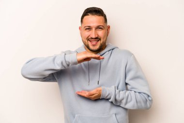 Beyaz arka planda izole edilmiş genç İspanyol adam iki eliyle bir şey tutuyor, ürün sunumu..