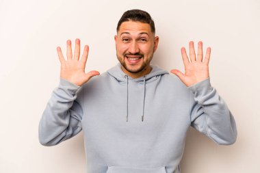 Latin kökenli genç bir adam beyaz arka planda izole edilmiş. Hoş bir sürprizle karşılaşıyor, heyecanlı ve el kaldırıyor..