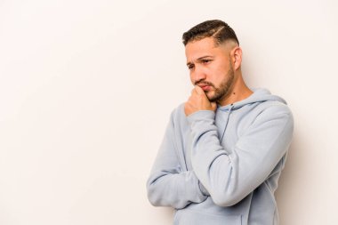 Beyaz arka planda izole edilmiş genç bir İspanyol şüpheli ve şüpheci bir ifadeyle yana bakıyor..