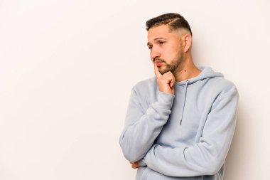 Beyaz arka planda izole edilmiş genç bir İspanyol şüpheli ve şüpheci bir ifadeyle yana bakıyor..