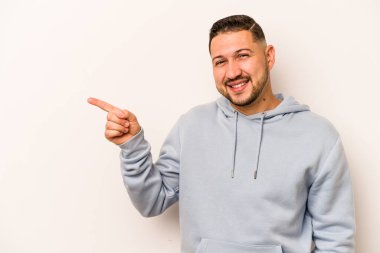 Beyaz arka planda izole edilmiş genç İspanyol adam işaret parmağıyla işaret ederek gülümsüyor..