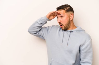 Beyaz arka planda izole edilmiş genç İspanyol adam uzaklara bakıyor ve elini alnına koyuyor..