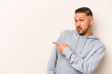 Beyaz arka planda izole edilmiş genç İspanyol adam gülümsüyor ve boş alanda bir şeyler gösteriyor..